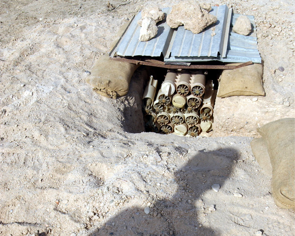 The shadow of a bomb disposal officer falls on a hidden store of mortar, Iraq, March 2003