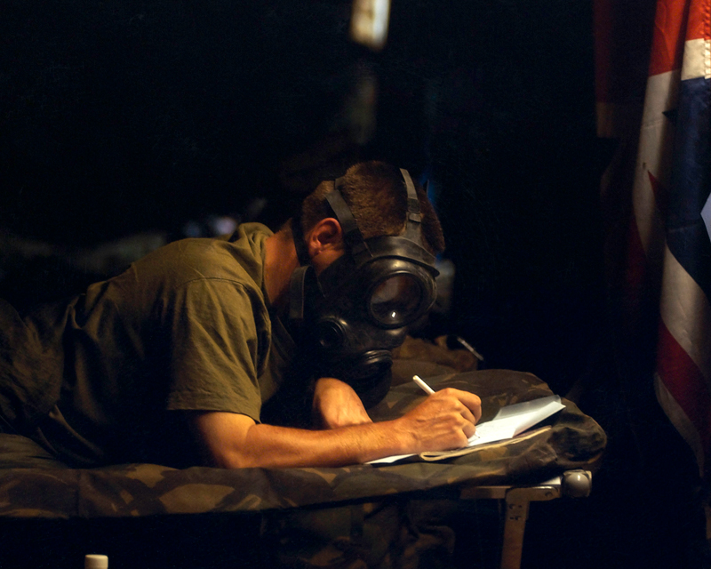 A soldier writes home during a chemical weapon alert in the Kuwaiti desert, 2003