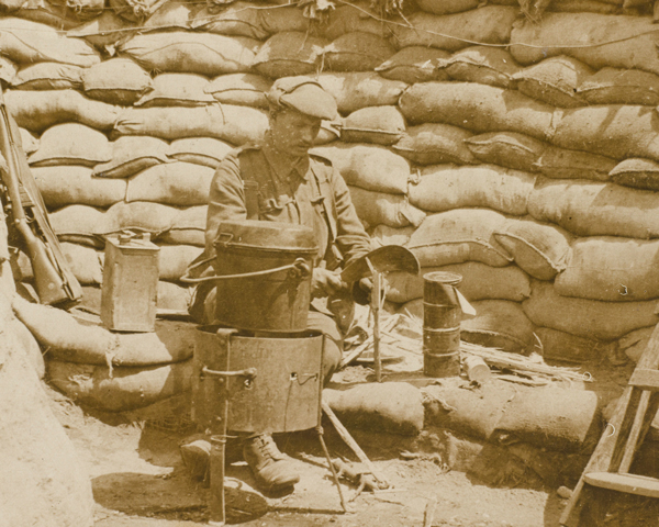 A cook preparing food in a dixie on a charcoal fire at the front, 1915