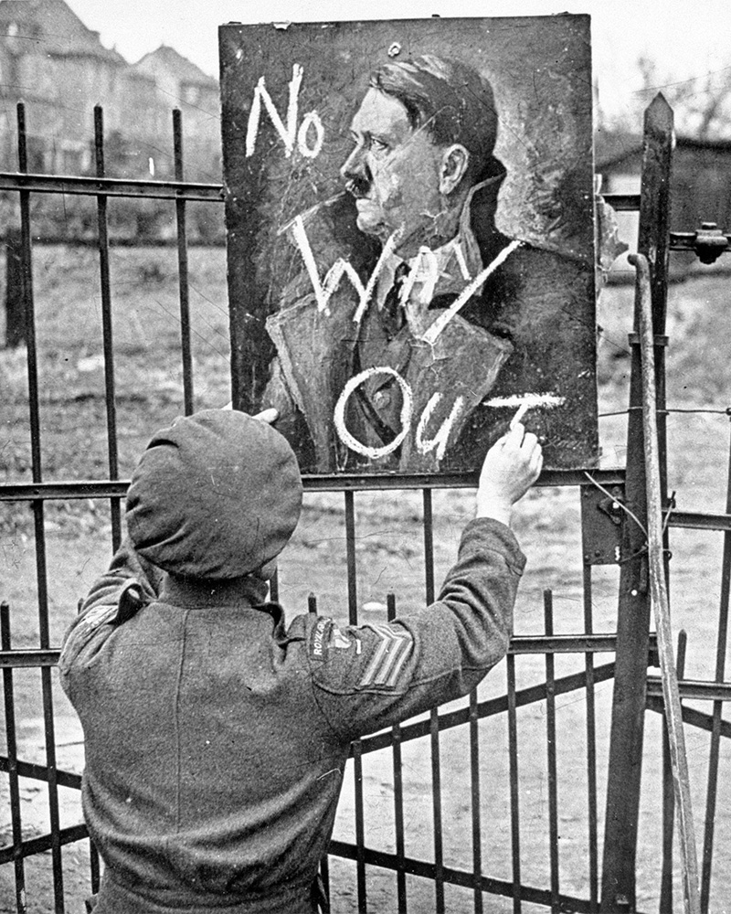 A British soldier writing ‘No Way Out’ on a portrait of Adolf Hitler, 1945