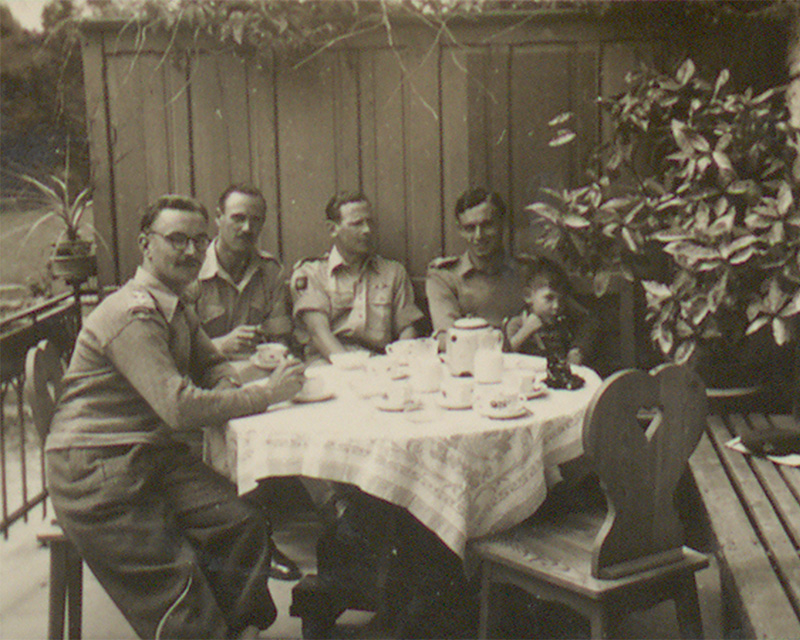 British soldiers and a small boy sitting around a table drinking tea, Trebesing, Austria, June 1945