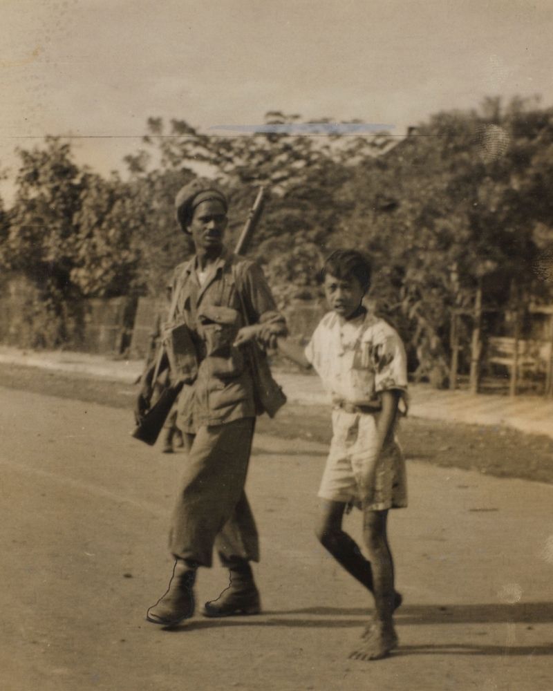 An Indian soldier walks a young Indonesian boy across a street by the wrist