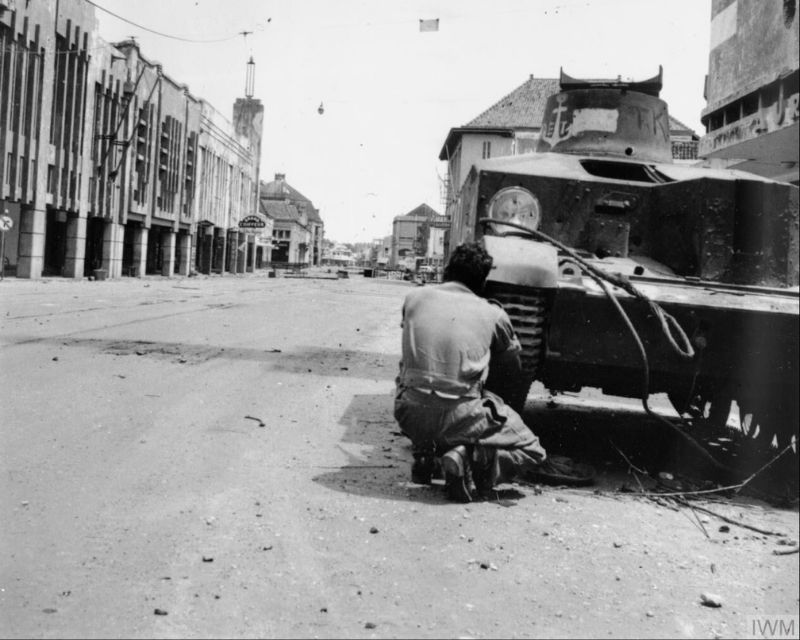 An Indian soldier uses a knocked-out Indonesian nationalist tank as cover in a main street in Surabaya during the fighting there