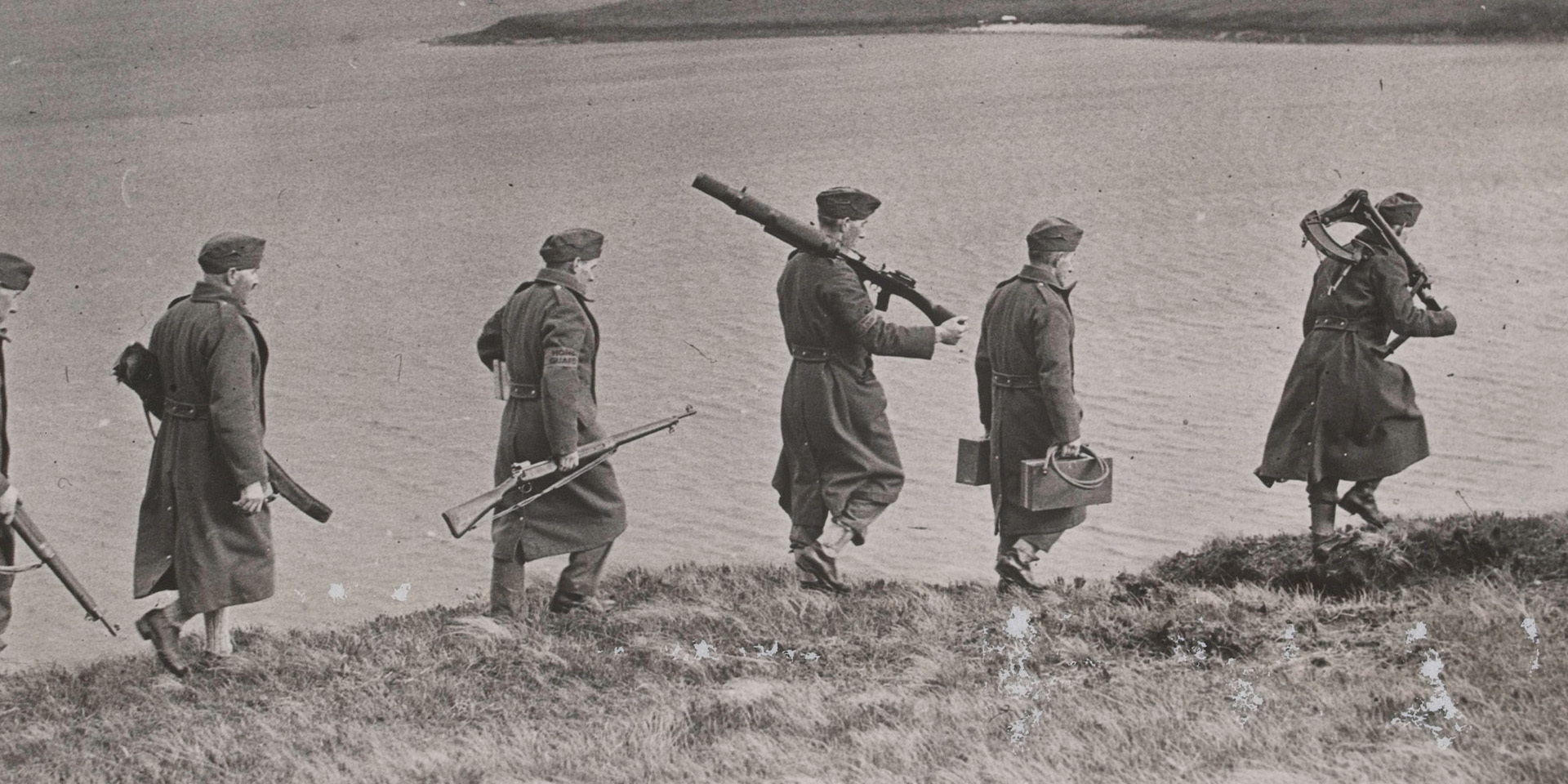 Home Guard soldiers carrying guns and equipment along a hillside in Scotland