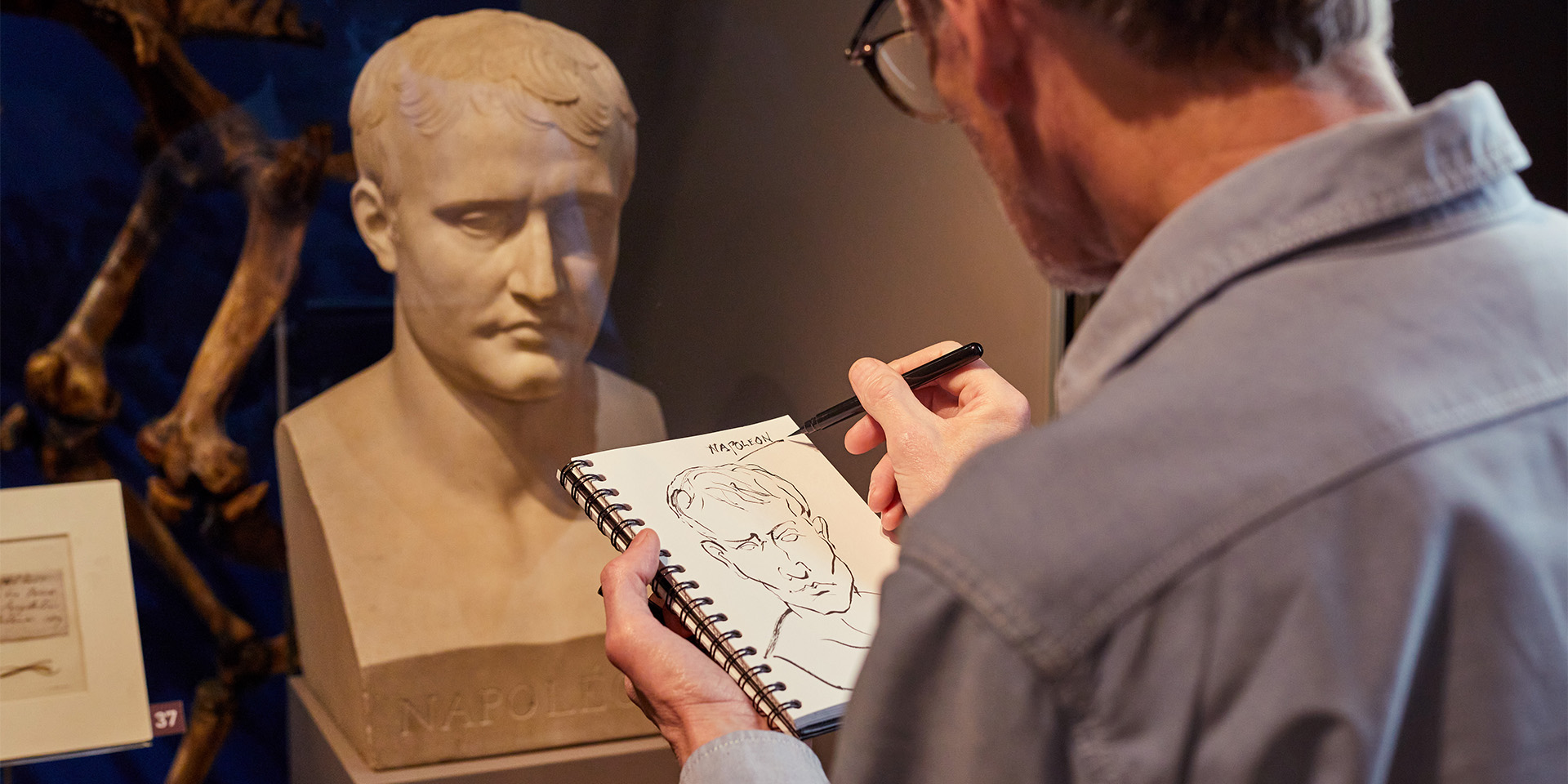 A museum visitor sketching a bust of Napoleon on display in a gallery