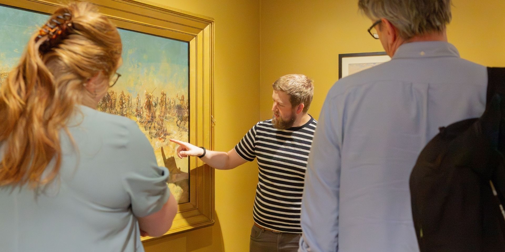 A man explaining a painting to two guests.