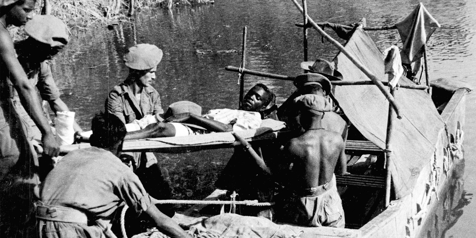 A wounded African soldier being carried by stretcher bearers on to a motor launch, Burma, c1944