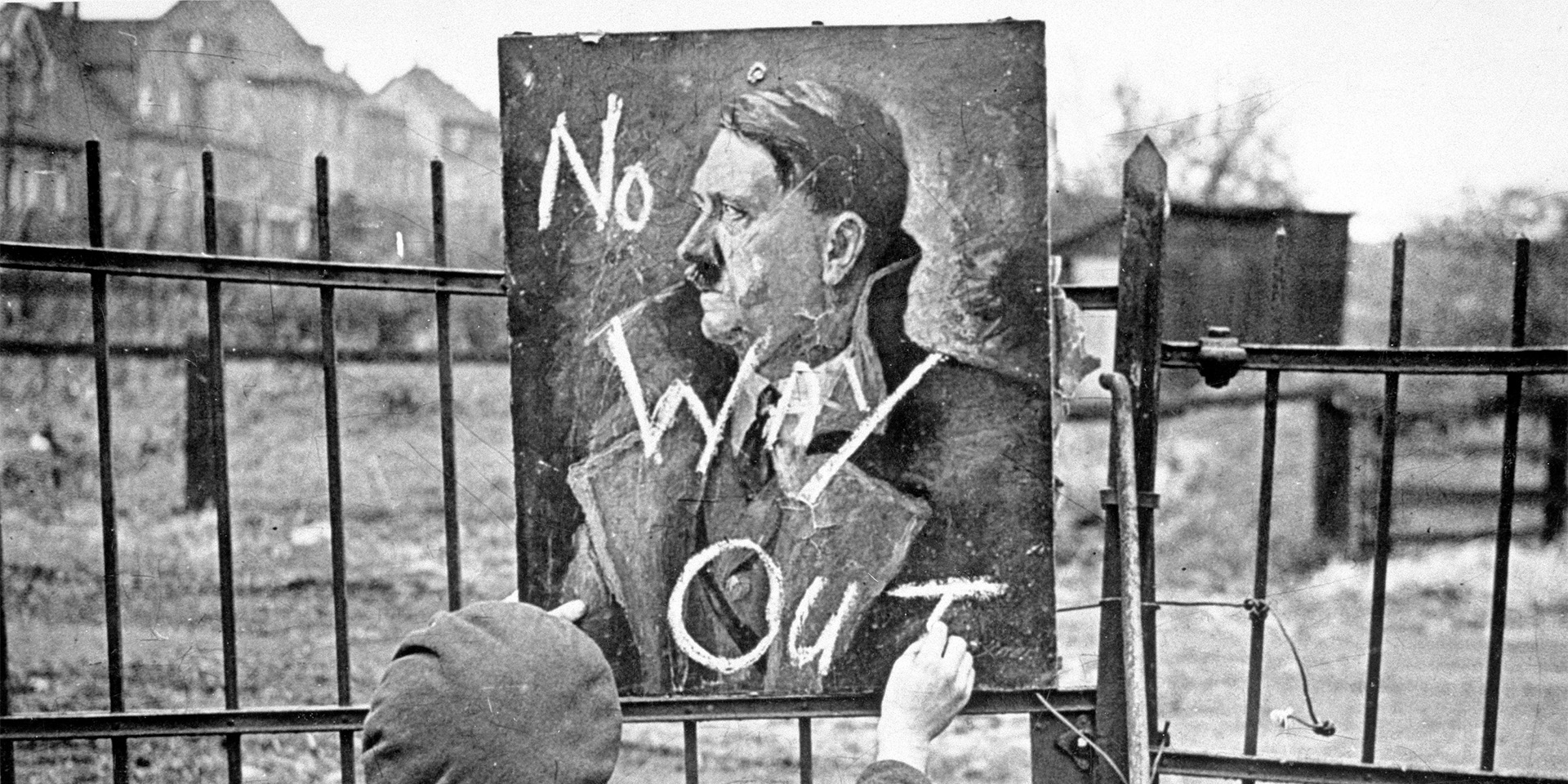 A British soldier writing ‘No Way Out’ on a portrait of Adolph Hitler, 1945
