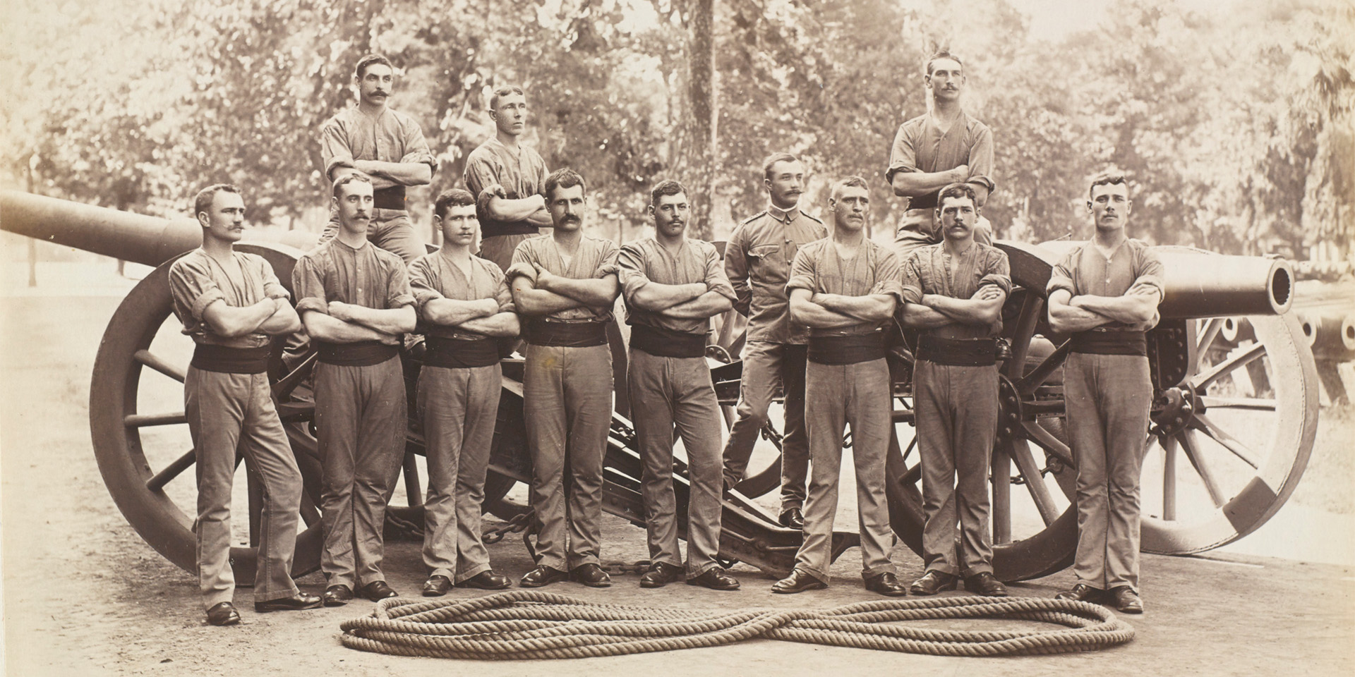 The 12 soldiers of the tug-of-war team of No 9 Company Eastern Division, Royal Garrison Artillery, in shirt sleeve order gathered round two howitzers, with rope on the ground in front of them, 1901