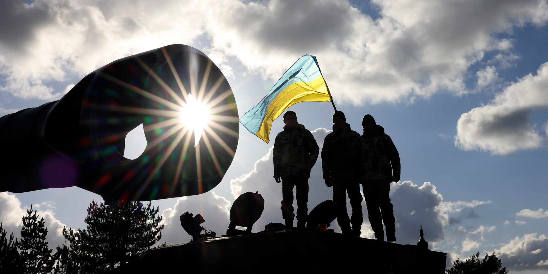 Silhouetted soldiers standing on an armoured vehicle with a Ukrainian flag 