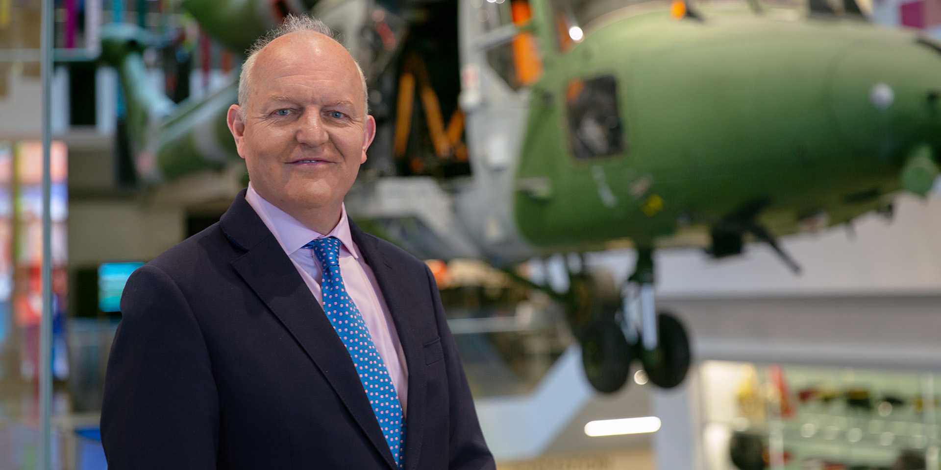 Justin Maciejewski in front of the Lynx helicopter in the Atrium at the National Army Museum