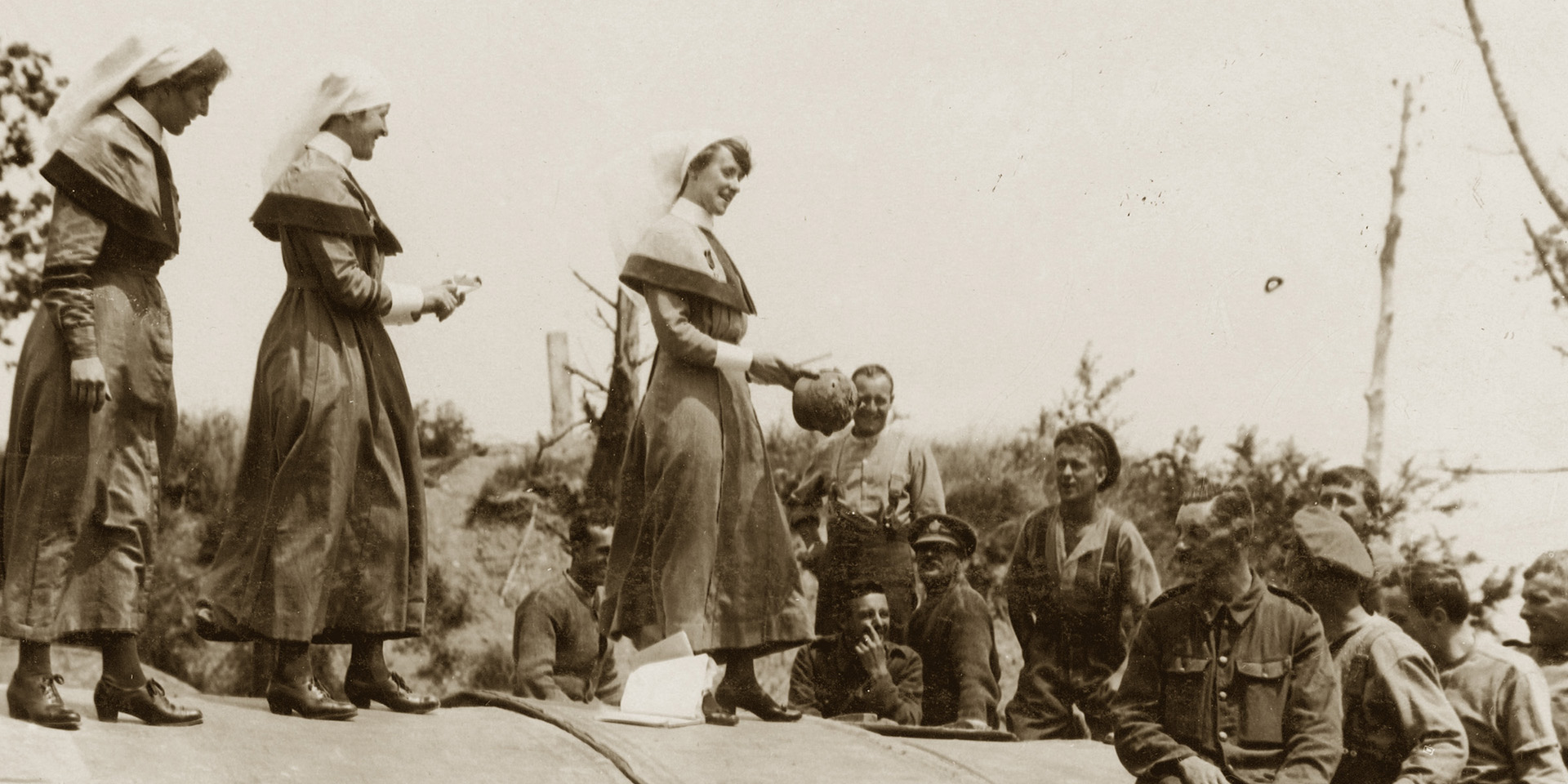 A Queen Alexandra's Imperial Military Nursing Service Reserve staff nurse and Territorial Force Nursing Service sisters auctioning a German steel helmet on a Hospital Barge, Peronne, 1917