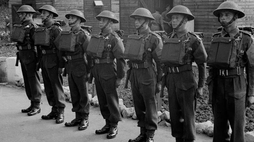 A parade of soldiers in helmets, gas mask cases on their chests and holstered revolvers at their sides
