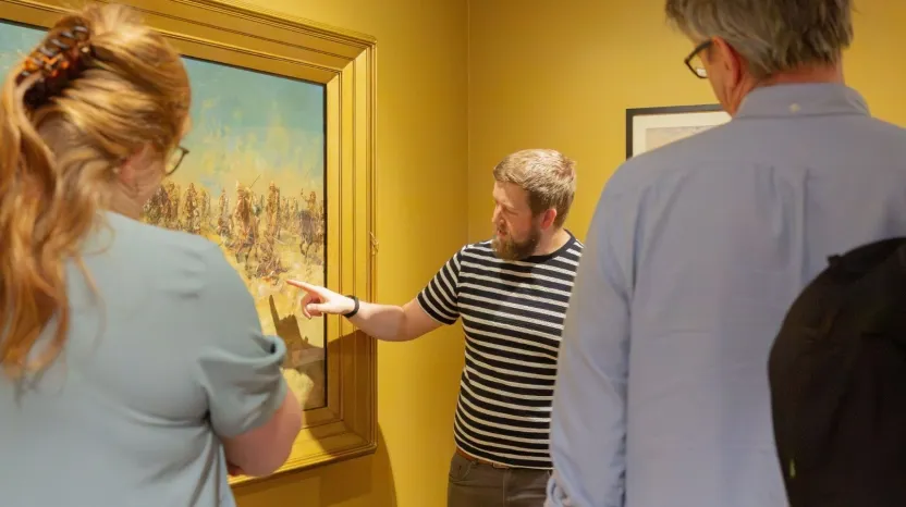 A man talking about a painting to two guests.