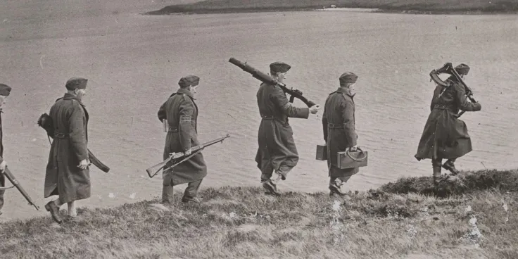 Home Guard soldiers carrying guns and equipment along a hillside in Scotland