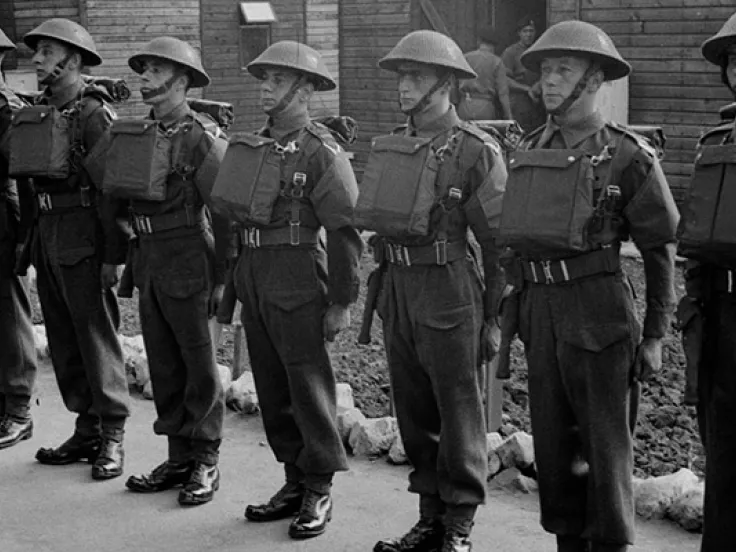 A parade of soldiers in helmets, gas mask cases on their chests and holstered revolvers at their sides