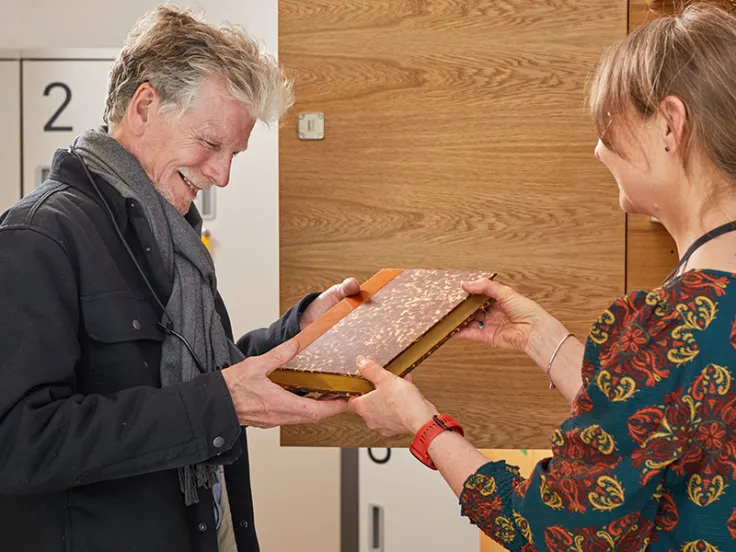 A visitor being presented with a bound book by a member of museum staff