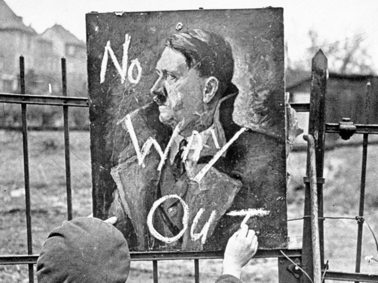 A British soldier writing ‘No Way Out’ on a portrait of Adolph Hitler, 1945