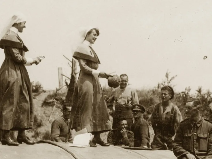 A Queen Alexandra's Imperial Military Nursing Service Reserve staff nurse and Territorial Force Nursing Service sisters auctioning a German steel helmet on a Hospital Barge, Peronne, 1917