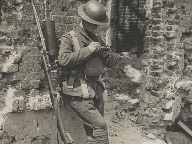 A soldier writing home while leaning against a ruined wall, Liévin, c1917
