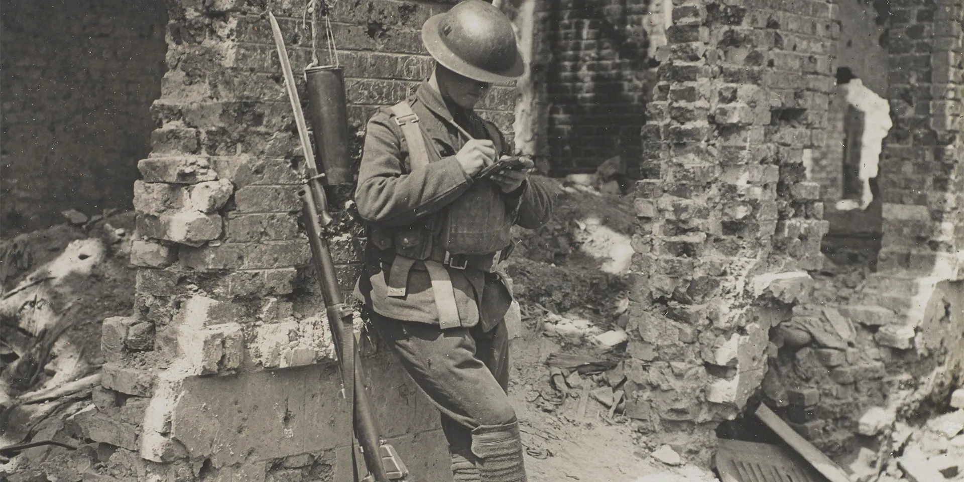 A soldier writing home while leaning against a ruined wall, Liévin, c1917