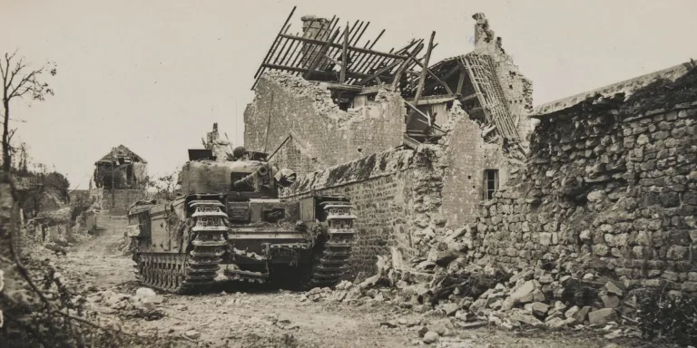 A Churchill tank awaits possible enemy counter-attack in a ruined village, 1944