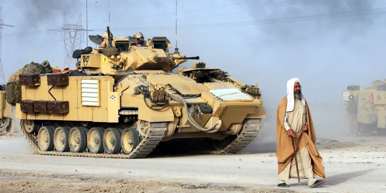 A civilian walks in front of a Warrior Infantry Fighting Vehicle, Iraq, March 2003